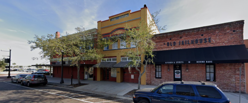 Colorful building with awnings and trees in front, alongside a brick structure with a sign for a bar and grill.