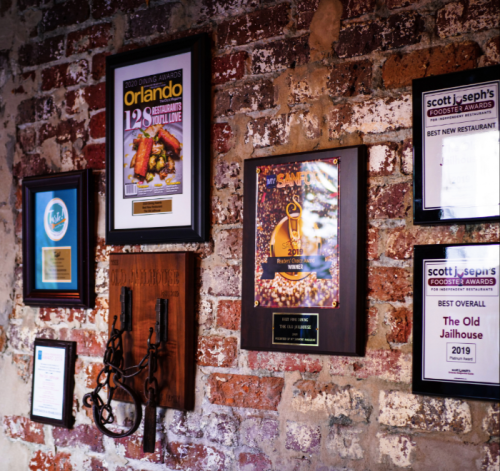 A brick wall displaying various awards and plaques, including "Best Overall" and "Best New Restaurant" honors.