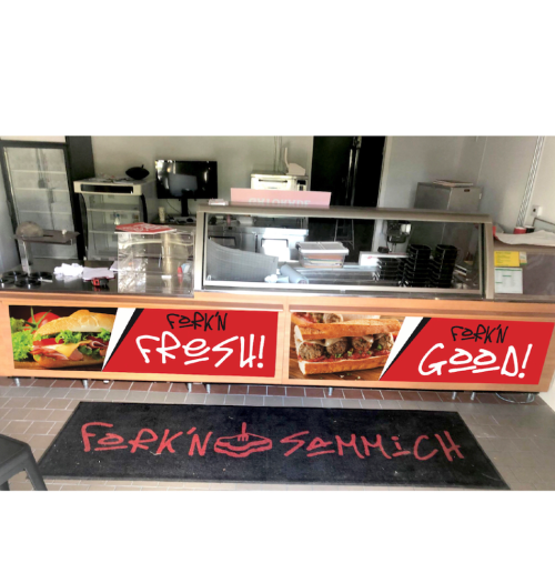 A food counter with a glass display, featuring bold signage that reads "FORK'N FRESH!!" and "FORK'N GOOD!"