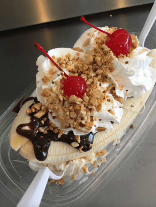 A delicious banana split topped with whipped cream, chopped nuts, chocolate sauce, and two cherries.