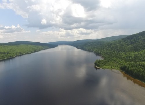 A serene lake surrounded by lush green hills under a cloudy sky, reflecting the landscape in calm waters.