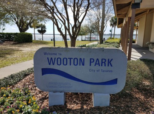 Sign welcoming visitors to Wooton Park in Tavares, with a view of the lake and trees in the background.