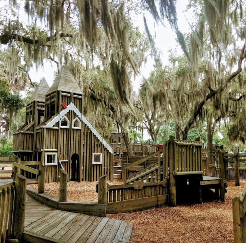 A wooden playground with towers and slides, surrounded by trees draped in Spanish moss.