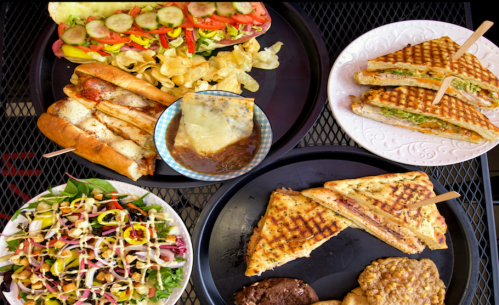 A variety of dishes including sandwiches, salad, chips, and a dessert on black trays.