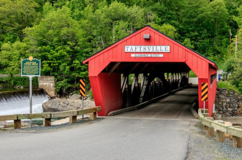 Red covered bridge in Taftsville, surrounded by green trees, with a sign indicating a 10-foot clearance.