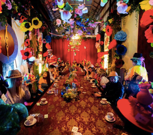 A vibrant, colorful dining room filled with flowers and decorations, with guests enjoying a festive meal at a long table.