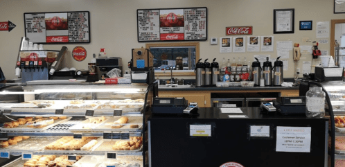 A bakery counter displaying various pastries, coffee machines, and a menu board in a cozy shop setting.