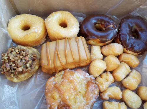 A variety of donuts and pastries, including glazed, chocolate, and a pecan-topped treat, arranged in a box.