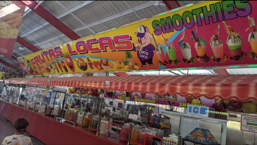 Colorful food stall with a vibrant sign for "Frutas Locas" and "Smoothies," featuring various fruit drinks and snacks.