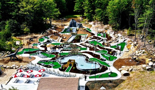 Aerial view of a mini-golf course featuring waterfalls, rocks, and lush greenery, surrounded by trees.