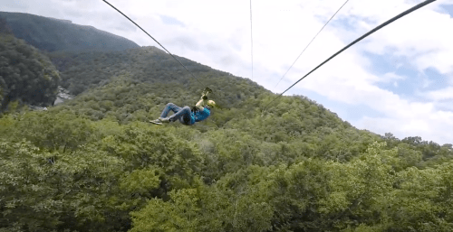 A person zip-lining over lush green mountains under a partly cloudy sky.