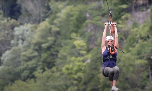A woman zip-lining through a lush green forest, smiling as she enjoys the adventure.