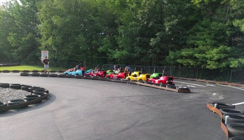 A row of colorful go-karts lined up on a racetrack surrounded by trees.