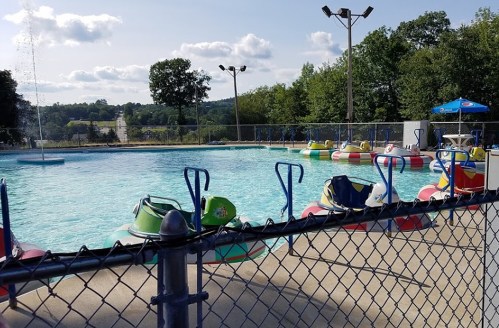 A fenced pool area with colorful paddle boats, surrounded by trees and a clear blue sky.