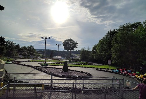 A go-kart track winding through a scenic outdoor area, with trees and a bright sun in the sky.