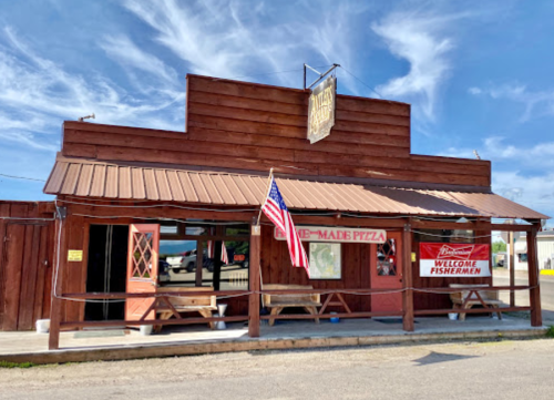 A rustic wooden building with a sign for homemade pizza and a welcome banner for fishermen, under a blue sky.