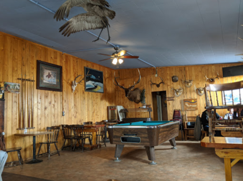 Cozy rustic interior of a restaurant with wooden walls, a pool table, and mounted animal heads on display.
