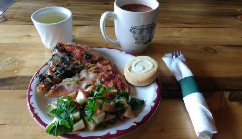 A plate with pizza, a salad, a cookie, and drinks: a mug of hot beverage and a glass of clear liquid on a wooden table.
