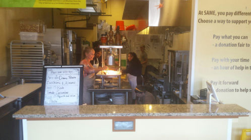 A busy kitchen with staff preparing food, a menu board, and various cooking equipment visible in a warm, inviting space.