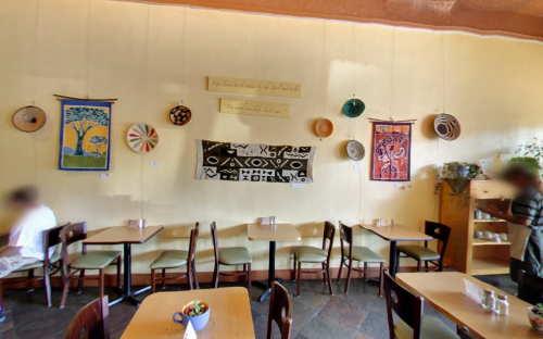 A cozy café interior with wooden tables, colorful wall art, and decorative baskets hanging on the walls.