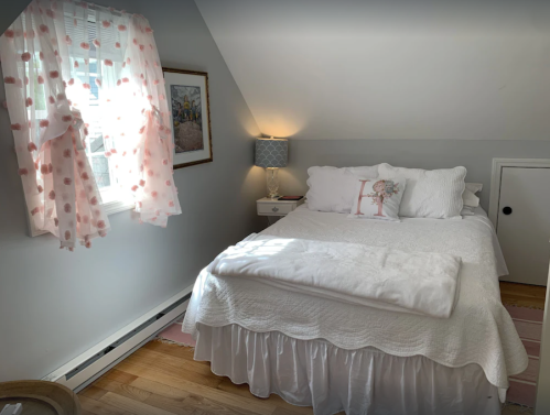 Cozy bedroom with a white bedspread, pink polka dot curtains, and soft lighting from a bedside lamp.