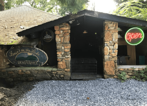 A rustic stone restaurant entrance with a neon "Open" sign and a sign reading "Louie's on the Lake."