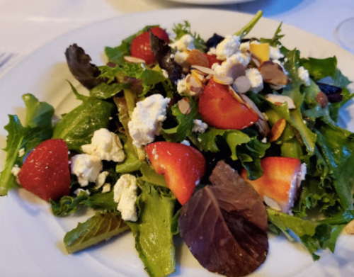A fresh salad with mixed greens, strawberries, almonds, and crumbled cheese on a white plate.