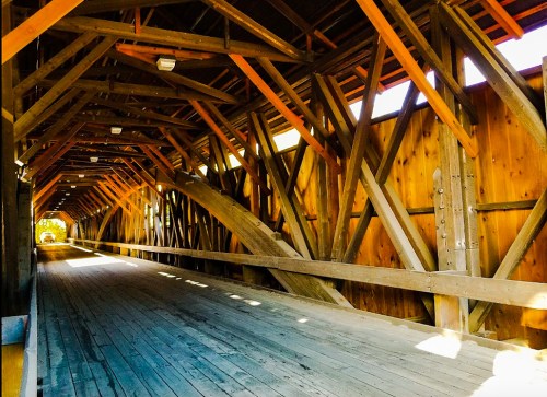 Interior view of a wooden covered bridge, featuring exposed beams and a wooden floor, illuminated by natural light.