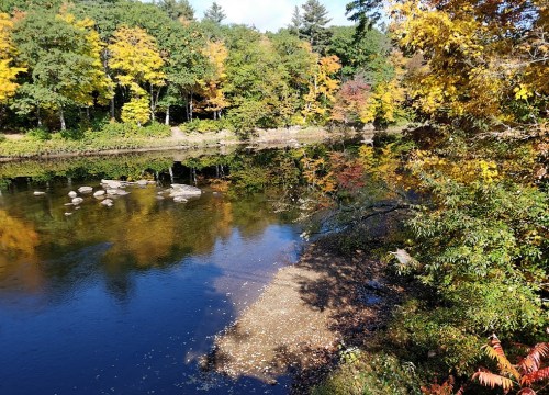 A serene river scene surrounded by colorful autumn trees and rocks, reflecting vibrant fall foliage in the water.