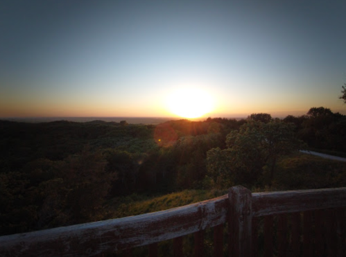Sunset over a lush landscape, with a wooden fence in the foreground and a clear sky transitioning to twilight.