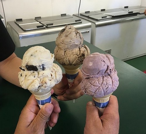 Three hands holding ice cream cones with different flavors: cookies and cream, chocolate, and raspberry.
