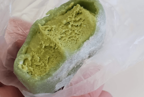 A hand holding a partially unwrapped green dessert with a smooth, creamy texture inside.