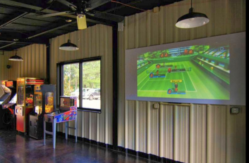 A game room featuring arcade machines and a large screen displaying a tennis video game.