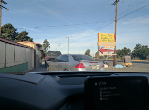 A car waits in line at a drive-thru near a sign for Peach Tree Produce & Coffee Shack.
