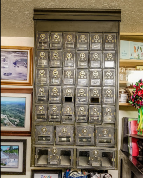 A vintage wall-mounted mailbox unit with multiple compartments, surrounded by framed photos and decorative items.