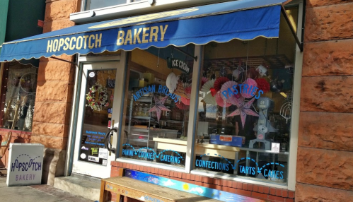 Exterior of Hopscotch Bakery with a blue awning, showcasing pastries and ice cream in the window.