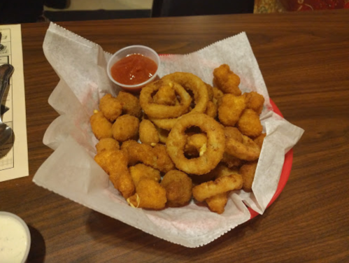 A basket of assorted fried appetizers, including onion rings and small breaded bites, served with dipping sauces.