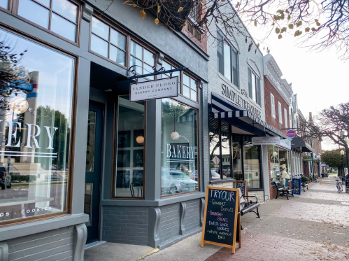 A charming street view featuring a bakery and a café with outdoor seating and a chalkboard menu.
