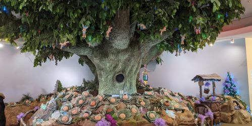 A large, whimsical tree with colorful decorations and small figures around its base, creating a magical scene.