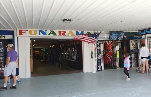 Entrance to Funarama arcade with slot machines inside, American flag hanging, and people walking by.