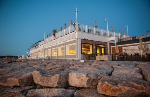 A seaside restaurant with outdoor seating, set against a twilight sky and rocky shoreline.