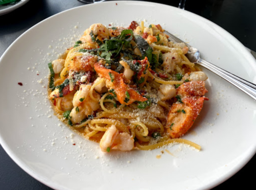 A plate of pasta with shrimp, lobster, herbs, and grated cheese, garnished with fresh basil.