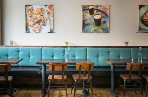 Cozy restaurant interior with teal seating, wooden tables, and food art on the walls. Fresh flowers on each table.