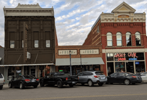 Historic buildings with shops and restaurants, featuring a mix of architectural styles and parked cars in front.