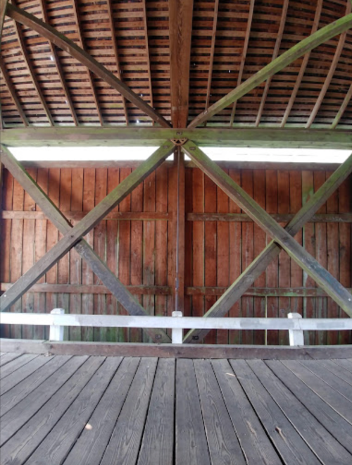 Interior view of a wooden structure with a slatted roof and cross-braced walls, featuring a wooden floor.