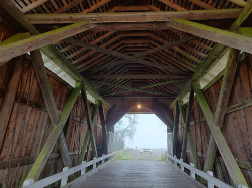 Interior view of a covered bridge with wooden beams and a misty landscape visible through the entrance.
