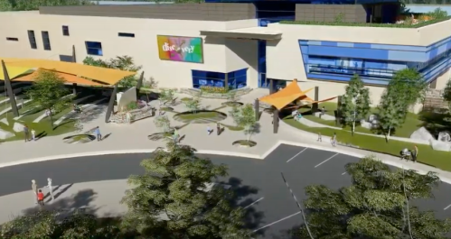 A modern building with colorful signage, surrounded by landscaped gardens and pathways, bustling with visitors.