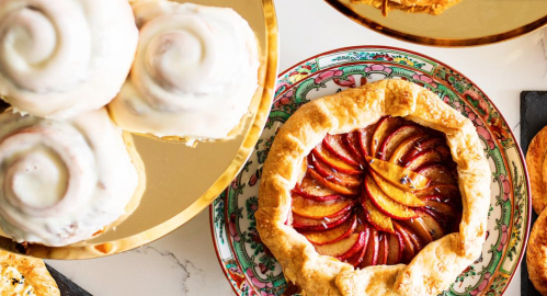 A colorful dessert spread featuring a fruit galette and cinnamon rolls on decorative plates.