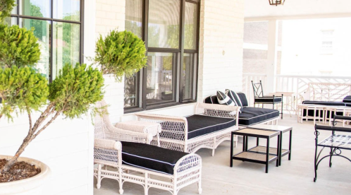 A cozy porch with black and white wicker furniture and potted greenery, creating a welcoming outdoor space.