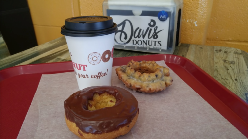 A tray with a coffee cup and two donuts: one chocolate-glazed and one with a crumbly topping.